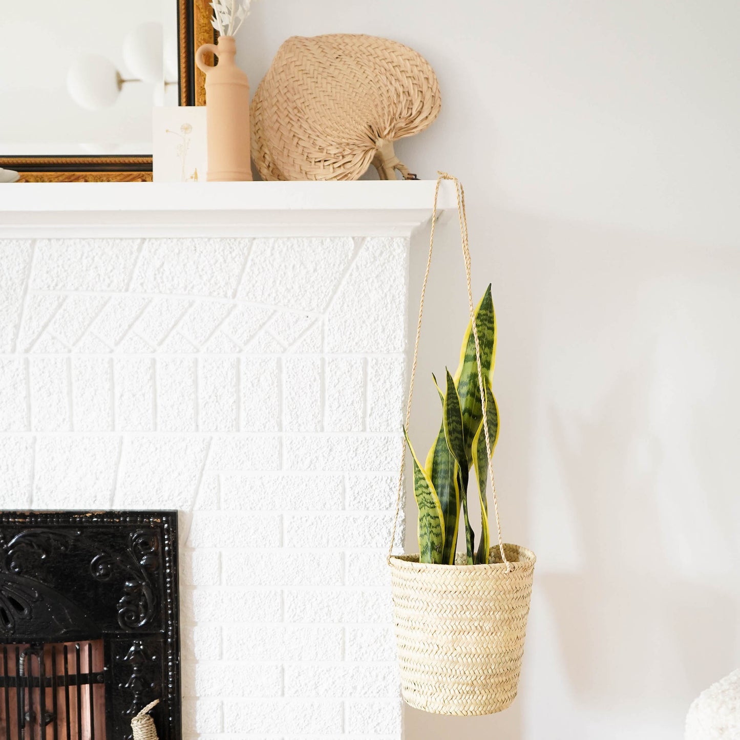 Straw planter holding a snake plant in front of a fireplace in a bright living room